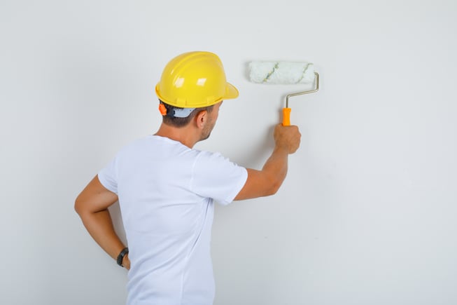 builder-man-painting-wall-with-roller-white-t-shirt-helmet-looking-busy-back-view